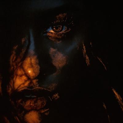 The primary subject of the image is a woman with long hair. She is looking at the camera with a focused expression. The setting is a dark room, and the visual style appears to be a black and white photo. The woman's hair is the main focus of the image, and the overall atmosphere is mysterious and captivating.